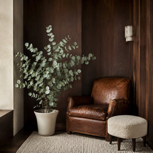 Eucalyptus artificiel 130 cm dans un coin lecture lambrissé, à côté d'un fauteuil en cuir patiné